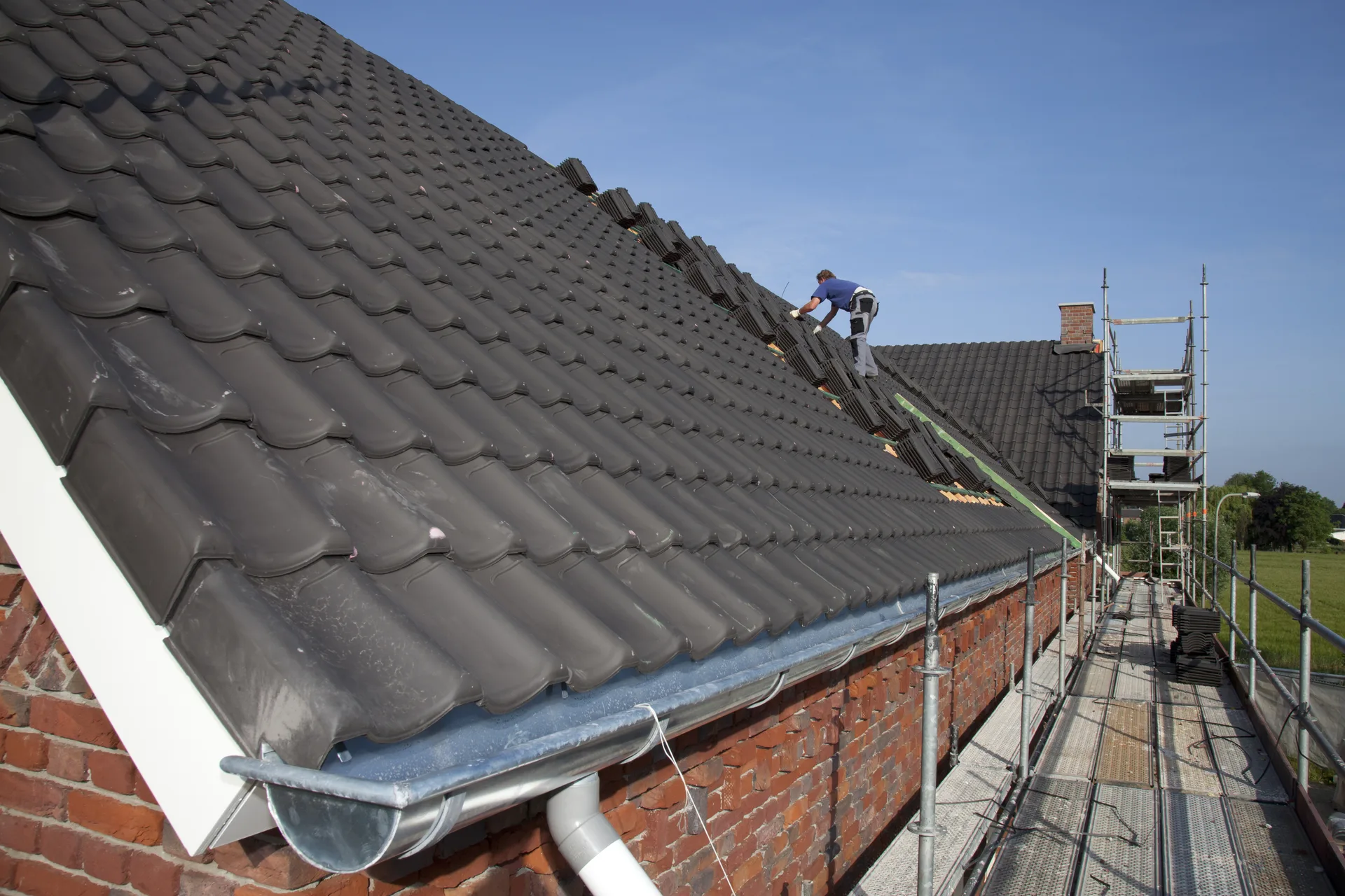 Roofer on the scaffold beside a run of new grey roof tiles and fresh guttering