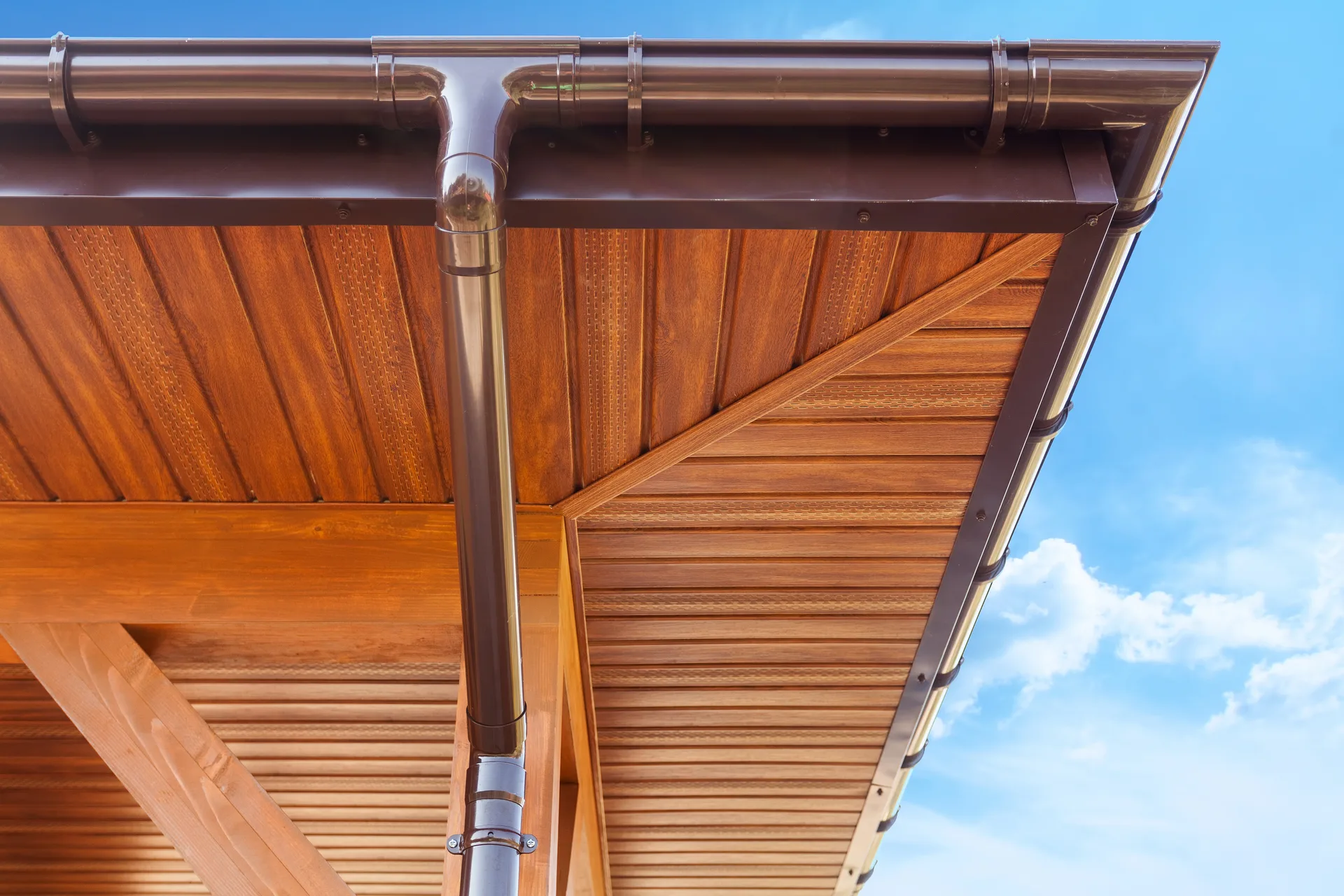 Brown guttering beneath timber-effect soffits against a blue sky