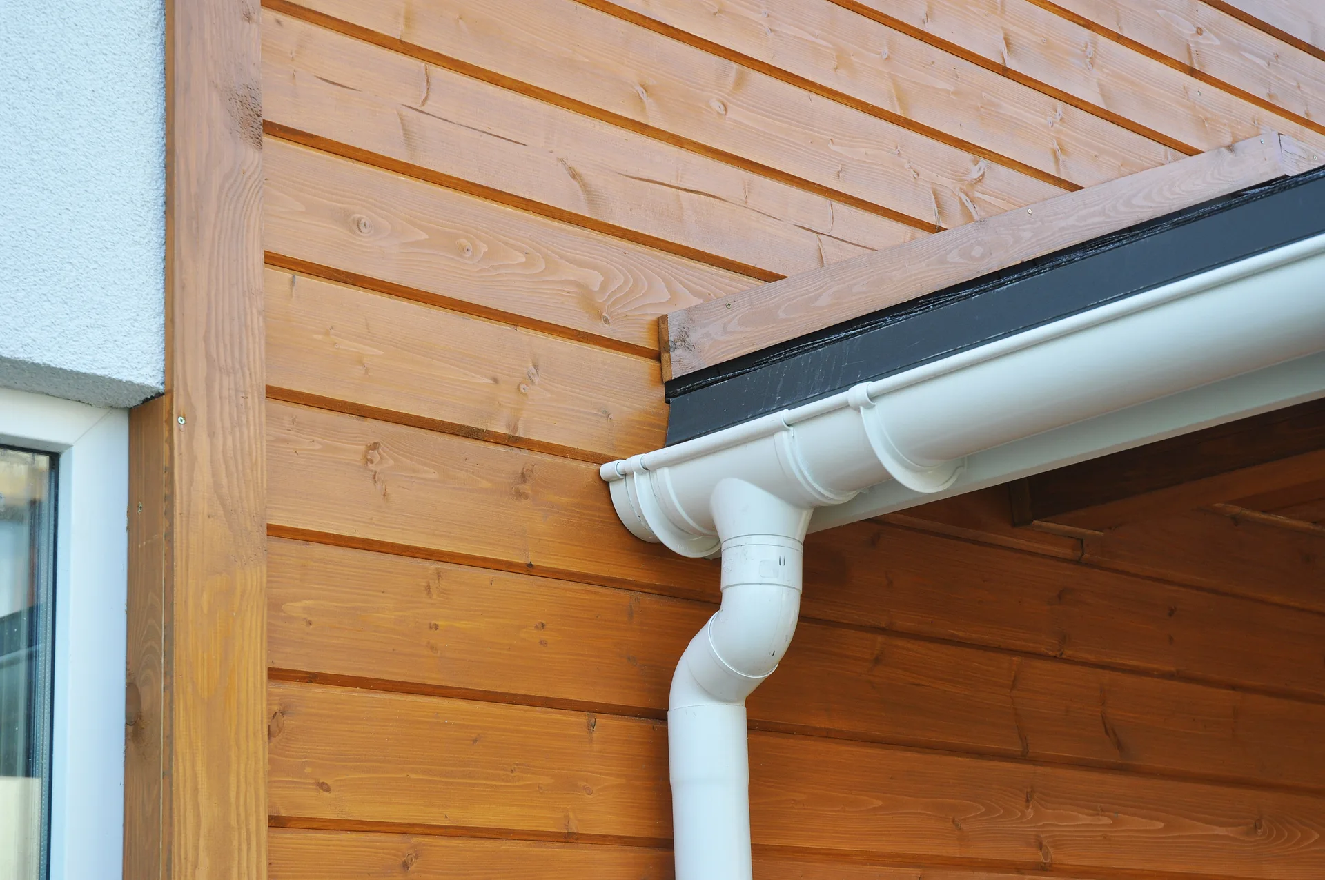 White uPVC gutter and downpipe fitted against timber cladding