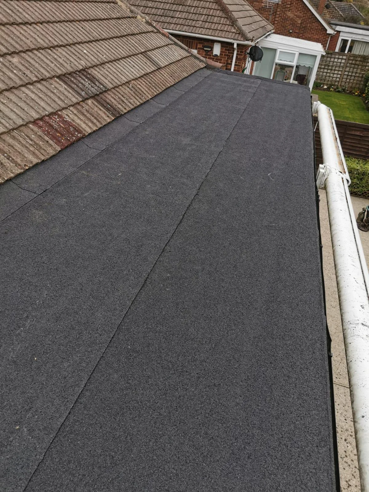 Newly laid dark flat roof on an extension, finished with a white gutter