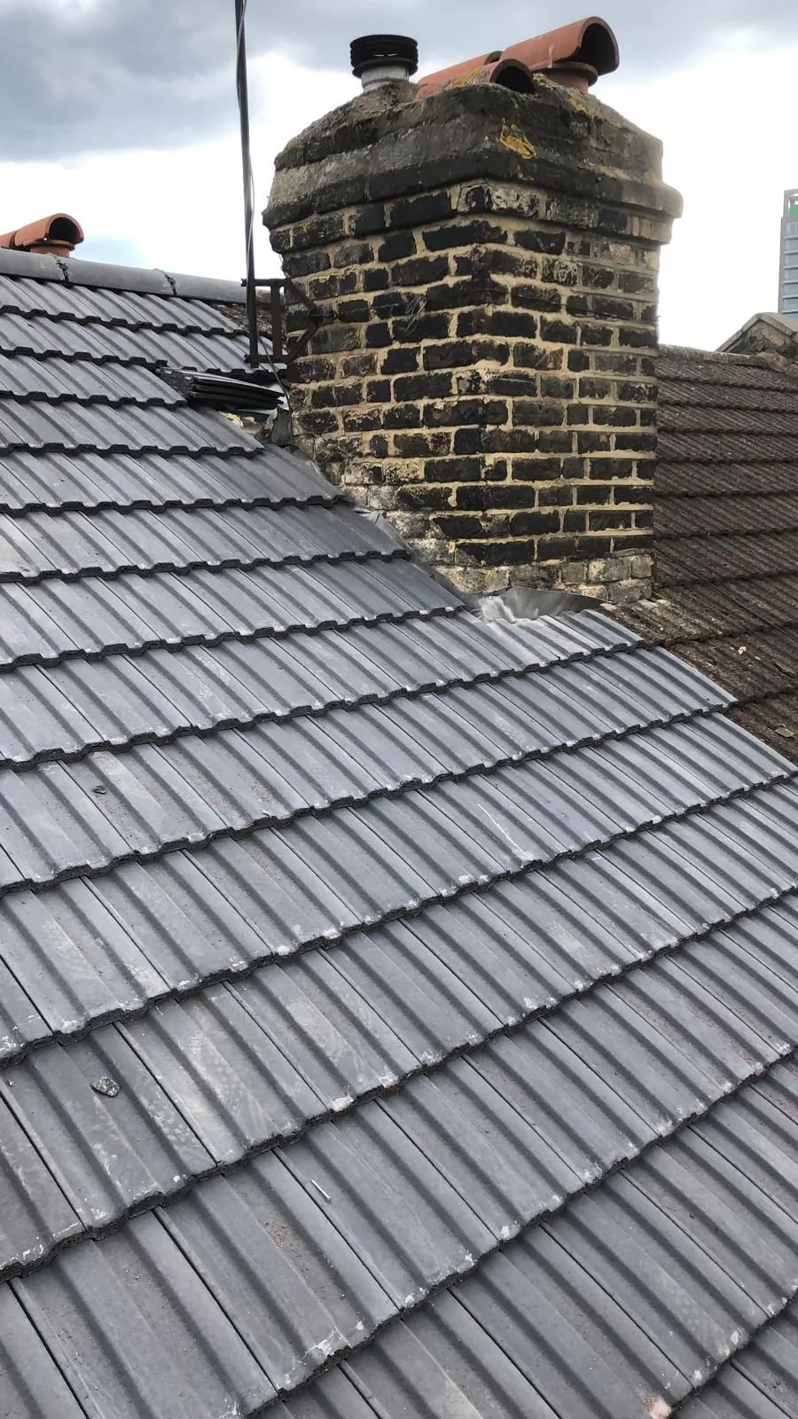 New grey roof tiles meeting a brick chimney stack