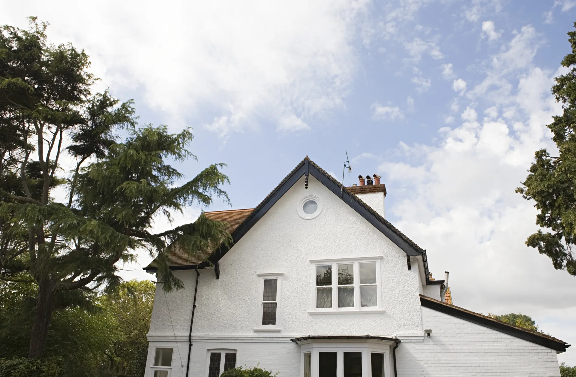 White rendered detached house with a steep gabled roof among trees