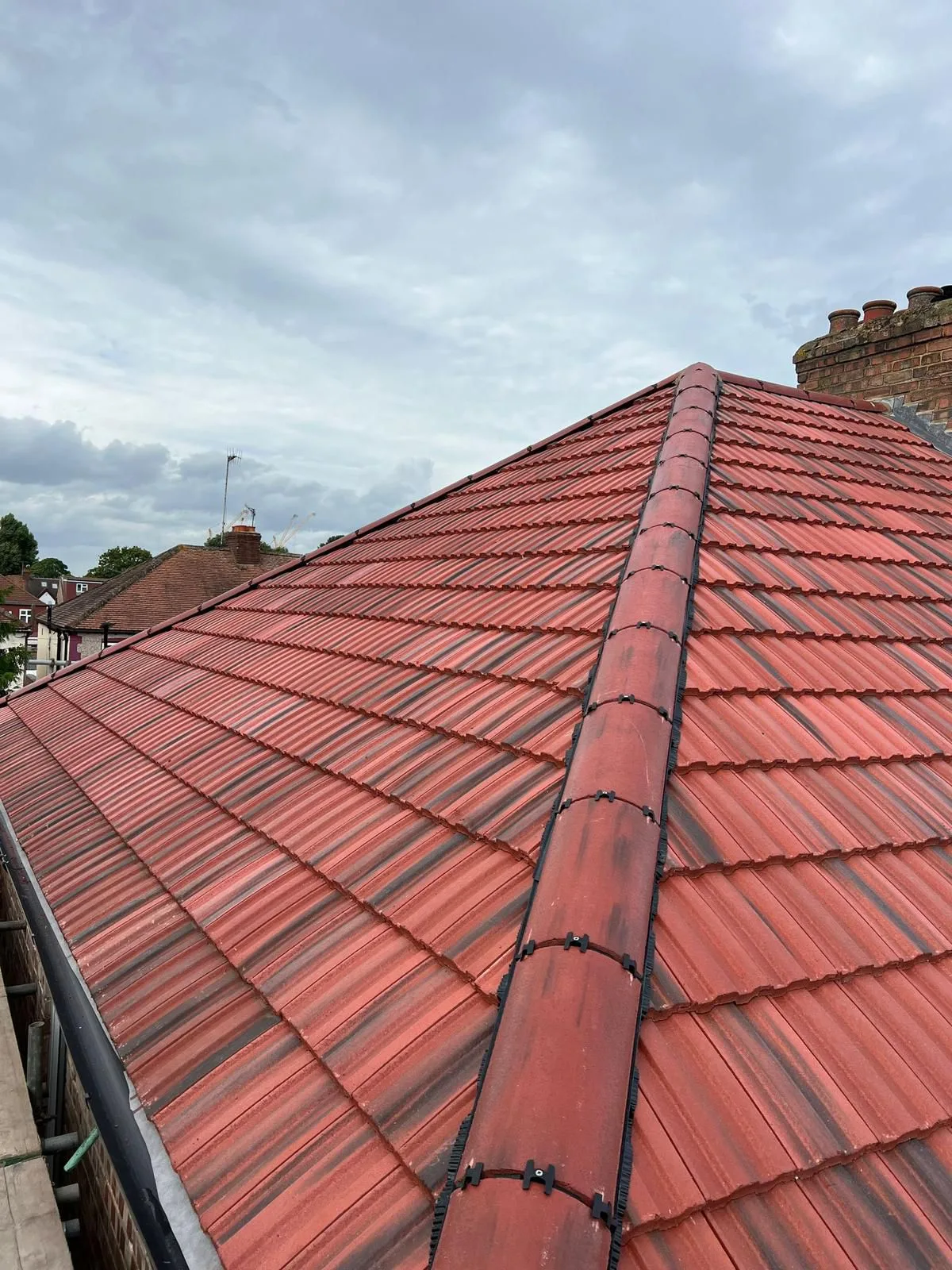 Newly tiled red hipped roof with a matching ridge, seen from the scaffold