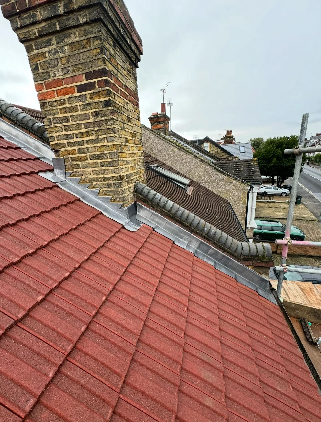 Brick chimney and lead-flashed abutment on a red tiled roof, seen from the scaffold
